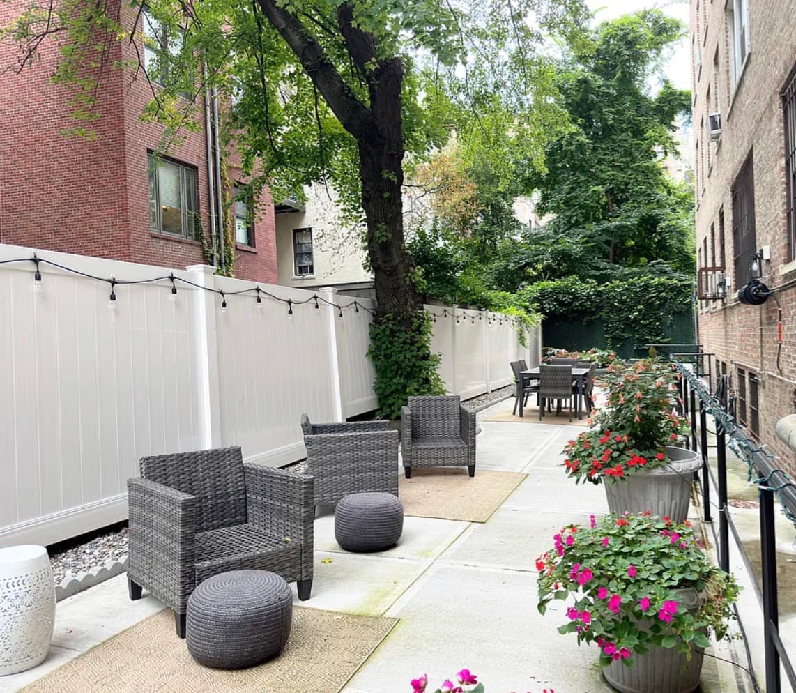 123 West 74th Street — the building's planted private rear garden: a paved patio with seating, string lights, container plantings, and a mature shade tree behind the pre-war facade