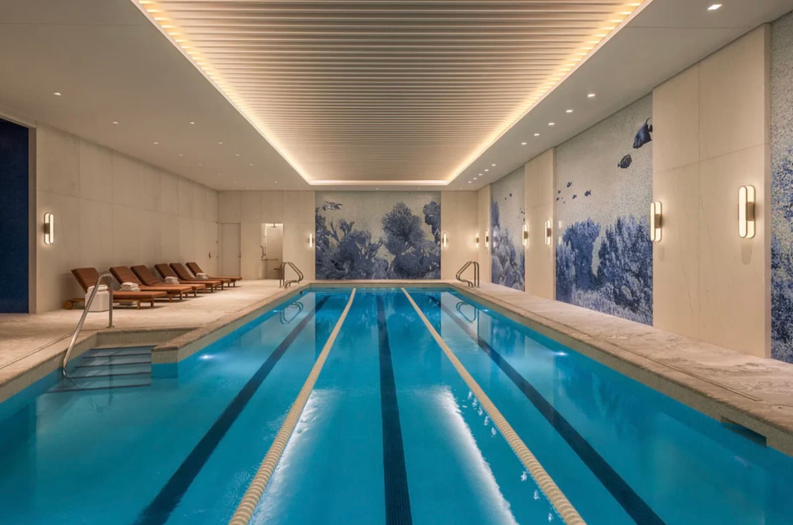 50 West 66th Street — the indoor saltwater lap pool, a three-lane marble-lined room with a slatted cove-lit ceiling and blue-and-white mosaic reef murals on the end and side walls