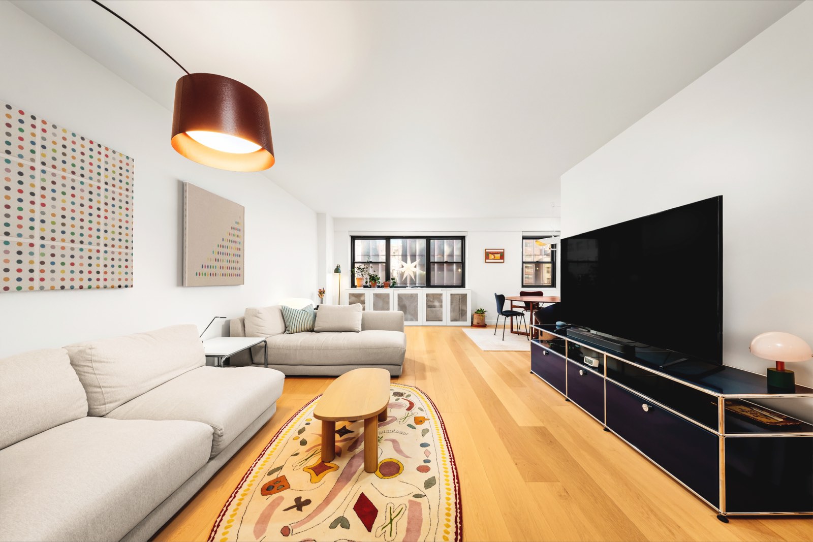 Lenox Manor #5E — the living room, with wide-plank oak floors running the length of the room to the dining area and the windows beyond