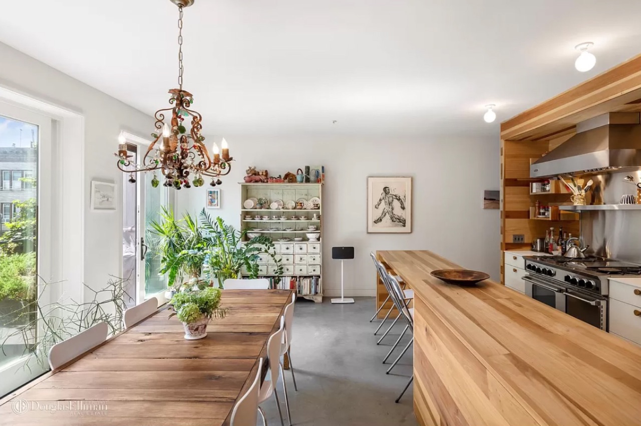 181 Richards Street — the kitchen-and-dining flow with the long live-edge dining table, the wood-clad kitchen at right with stainless professional range, the floor-to-ceiling glass doors to the rear deck, and the polished concrete flooring through the principal living level