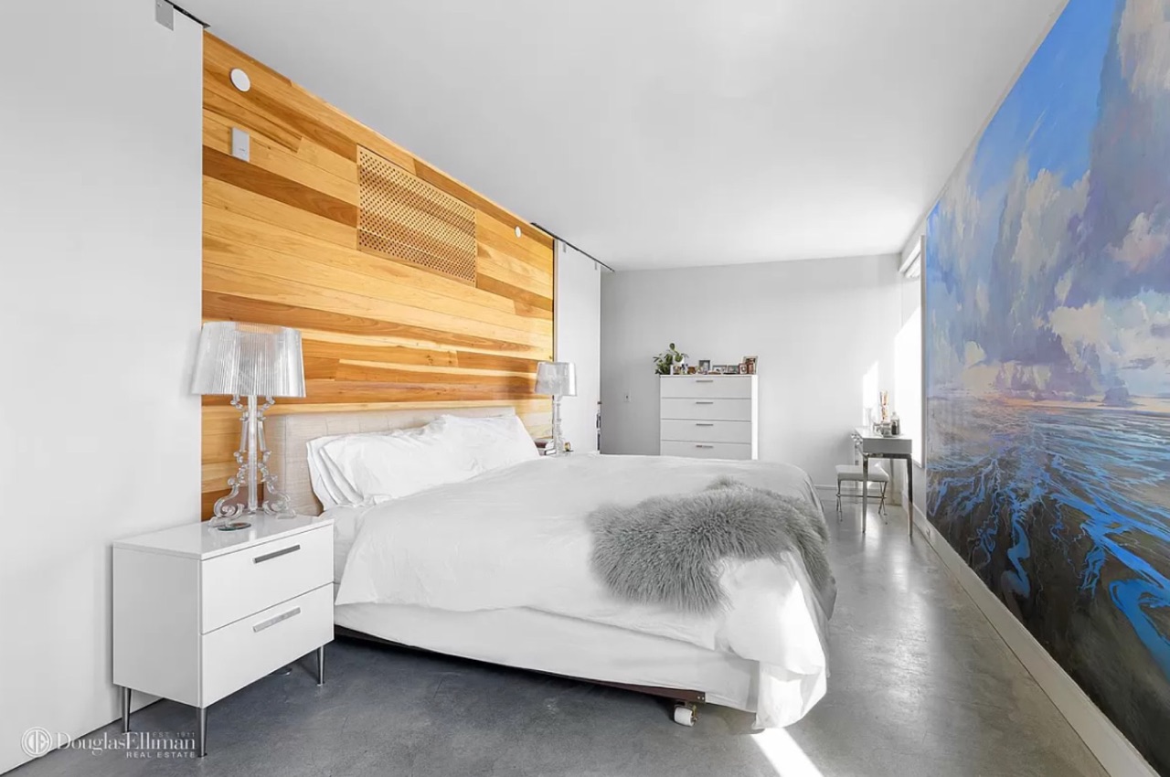 The primary bedroom — striking poplar wood headboard wall, large abstract ocean-themed mural artwork on the right wall, white nightstands, king bed with white linens, polished concrete floor
