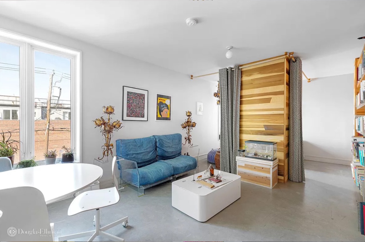 The office/study — denim futon couch, wood-clad room divider with grommet-curtain panels, contemporary art prints, the eclectic design-forward register the residence carries through the upper levels
