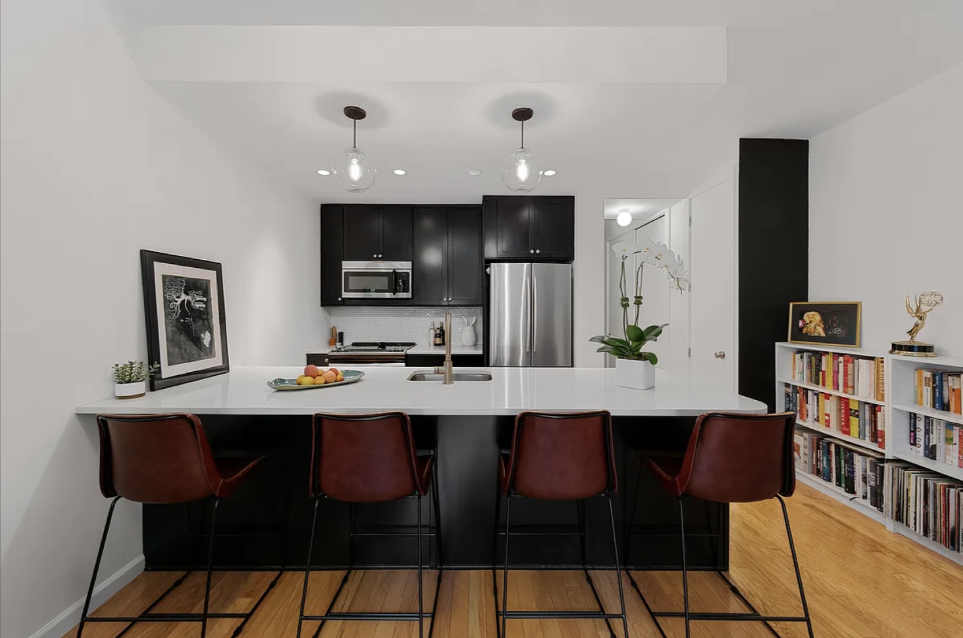 376 West Street #GB — modern open kitchen with black cabinetry, white quartz waterfall island, leather counter stools, and integrated library shelving