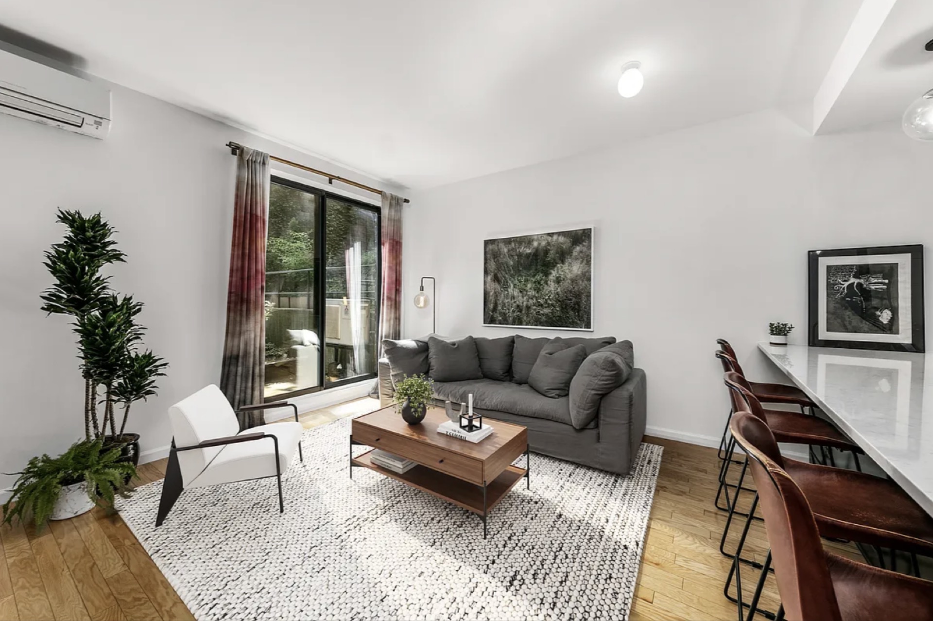 Living room with sliding-glass doors to the private garden — grey sectional, modern furnishings, layered area rug, light flooded through the garden-facing exposure