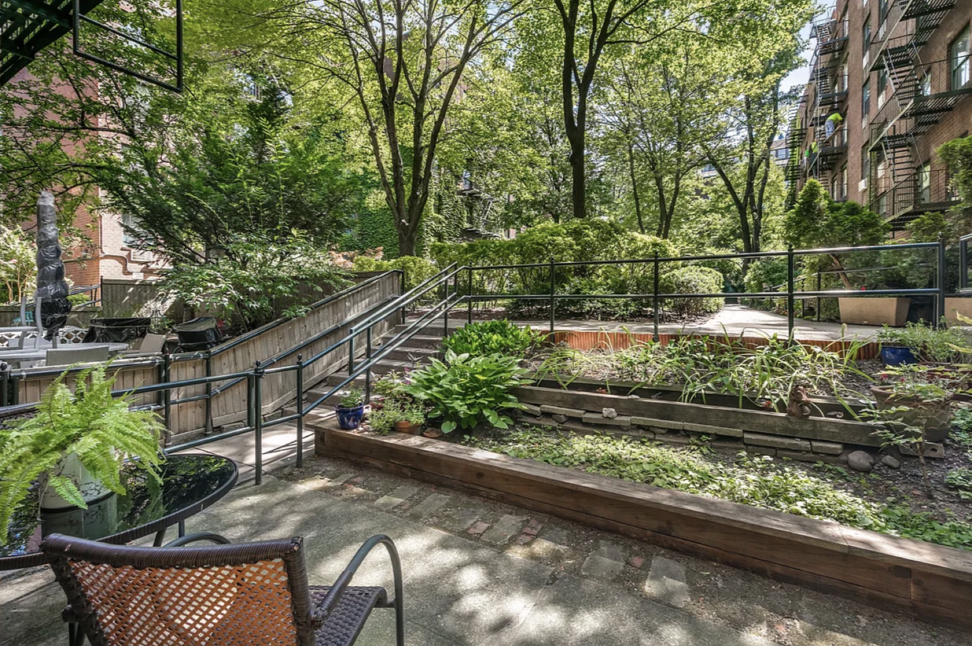 The private garden — mature tree canopy, raised planting beds, brick paver patio with wrought-iron furniture, the outdoor-program asset that defines Residence GB