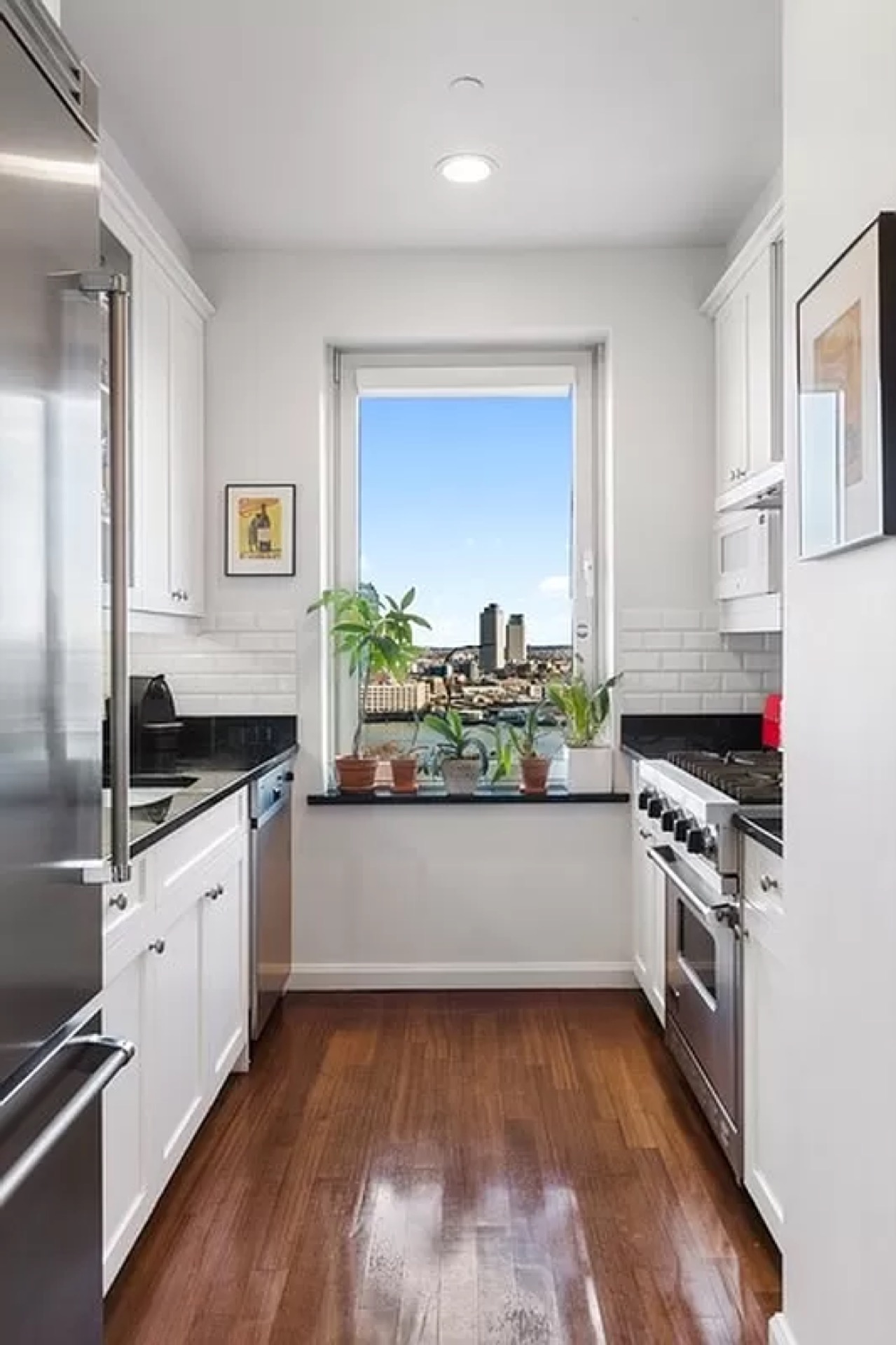 The galley kitchen — white shaker cabinetry, stainless professional appliances, city-view window over the work counter