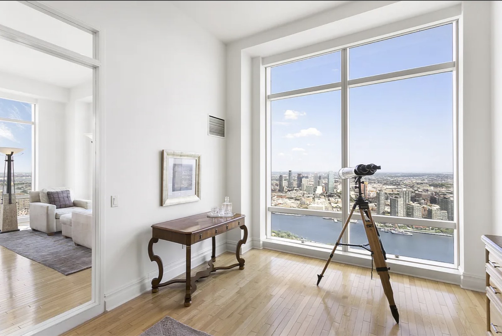 The office, with a floor-to-ceiling window over the East River and Long Island City, and a glass-paneled opening to the adjoining room