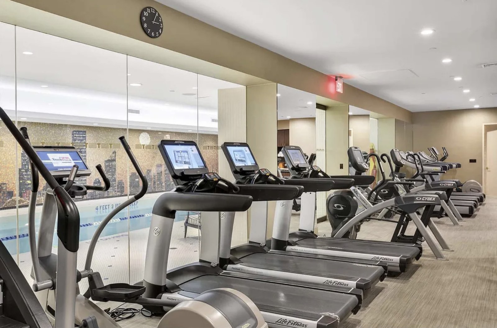 The fitness center at 845 United Nations Plaza, with a row of treadmills and cardio machines and a glass wall onto the pool